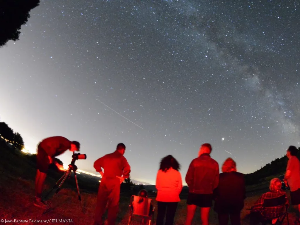 photo d'un groupe de personnes de tous âges en train d'observer le ciel à l'oeil nu ou au télescope